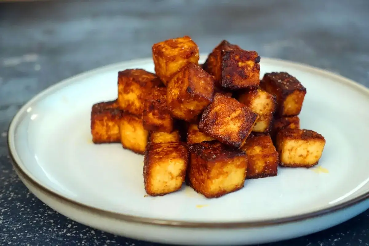 Knusprig gebratene Tofuw&uuml;rfel auf einem Teller. Perfekt, um Tofu knusprig zu braten und als leckere Beilage zu genie&szlig;en.