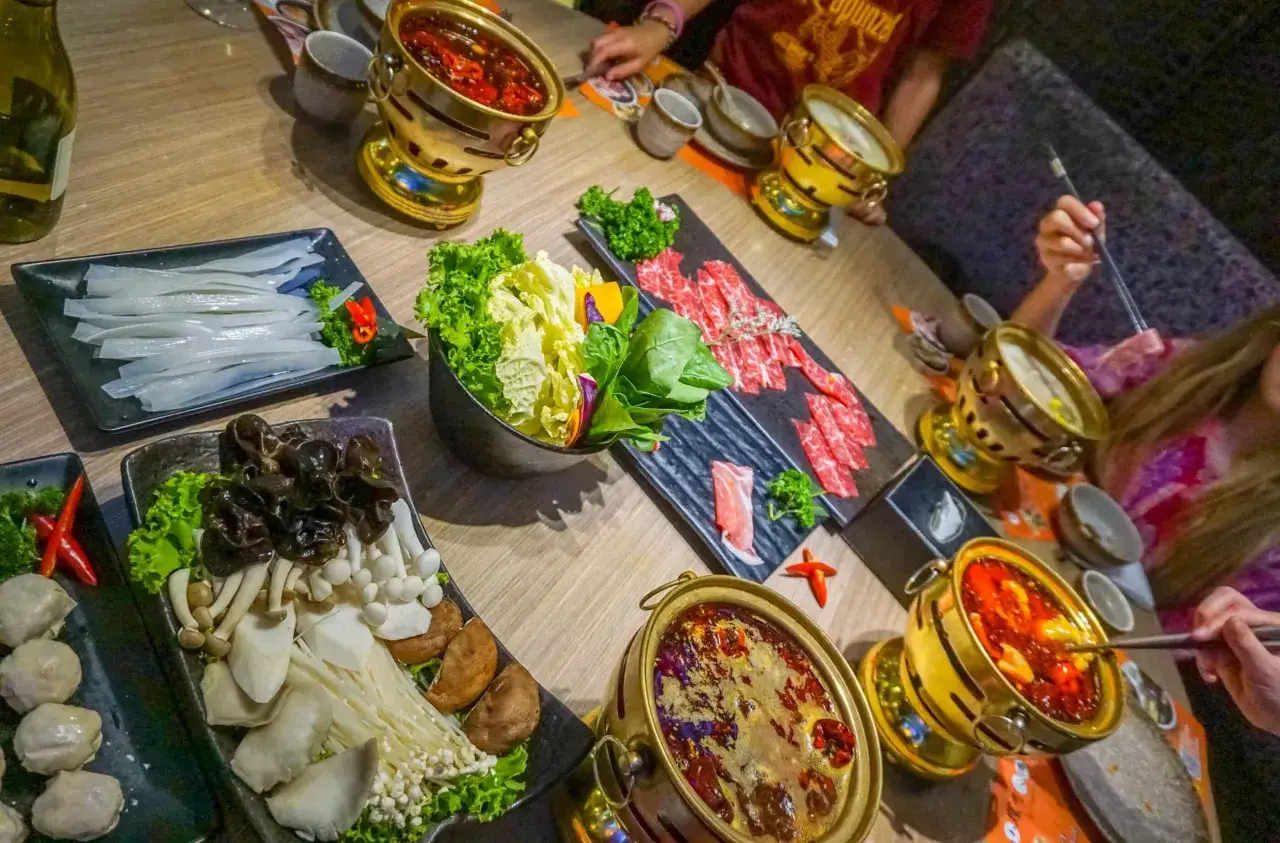 Ein Tisch voller Köstlichkeiten: Was ist Hot Pot? Hier brutzeln Brühen in goldenen Töpfen, umgeben von frischem Gemüse, dünn geschnittenem Fleisch und Pilzen.