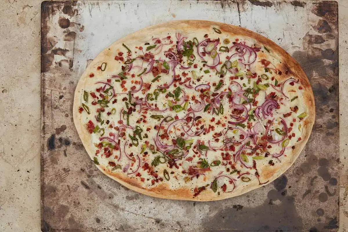 Flammkuchen mit klassischem Belag: Speck, Zwiebeln und Lauch auf cremiger Basis.