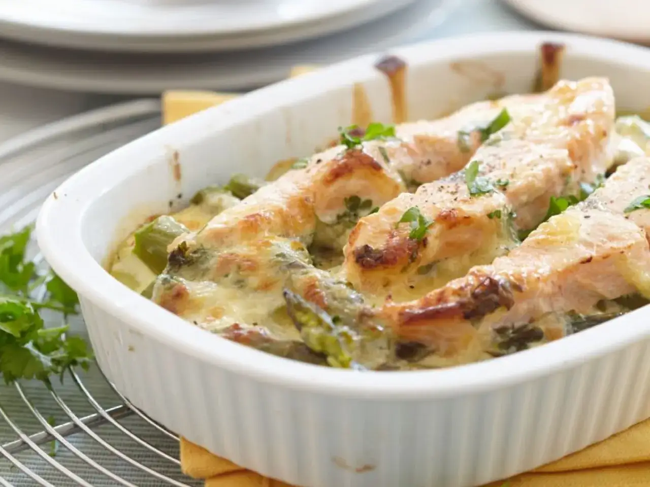 Ein köstlicher Spargel Lachs Auflauf mit geschmolzenem Käse und frischer Petersilie in einer weißen Auflaufform.