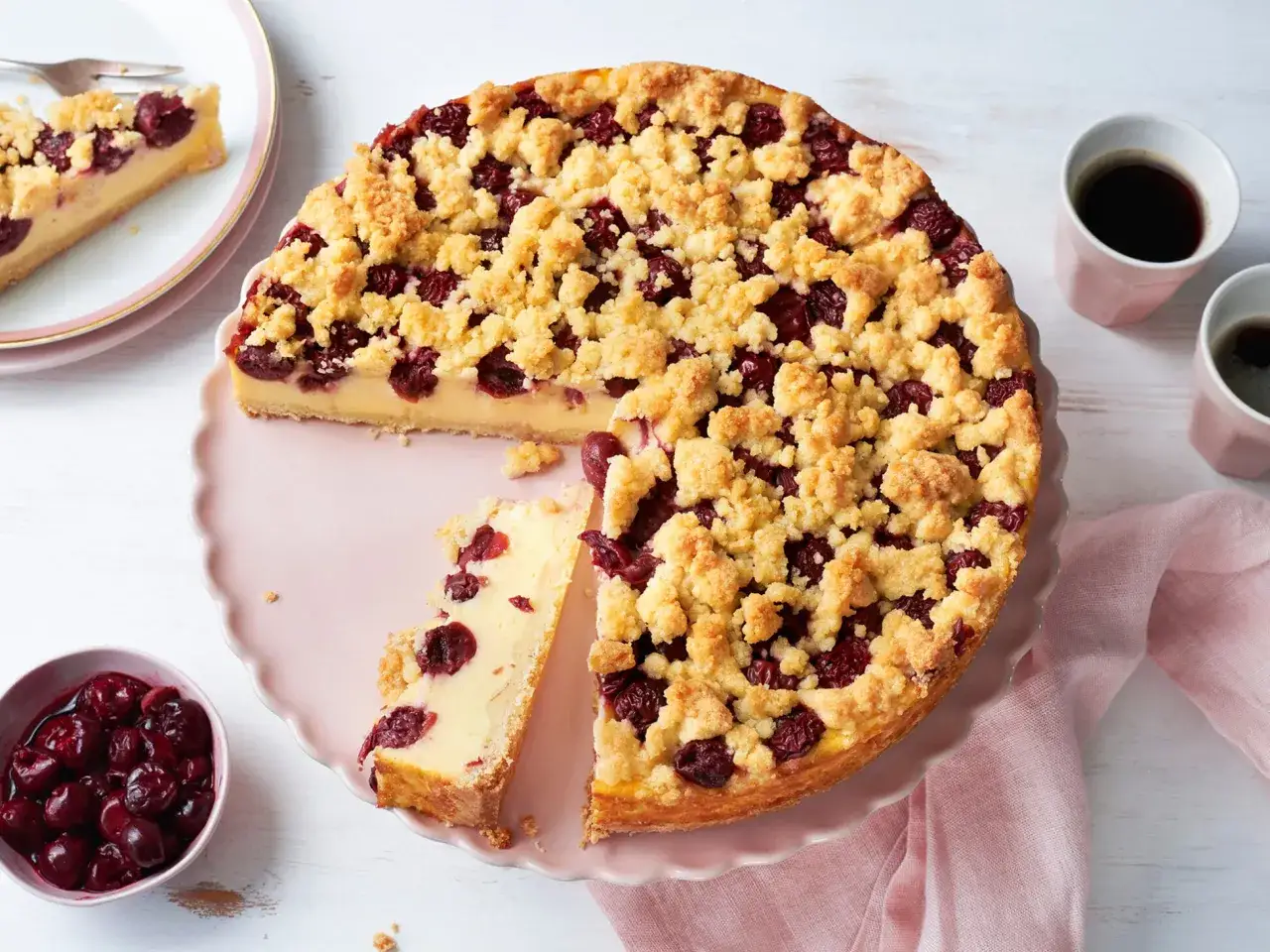 Ein saftiger Kirschkuchen mit Puddingf&uuml;llung und knuspriger Streuseldecke, serviert auf einer rosa Tortenplatte.
