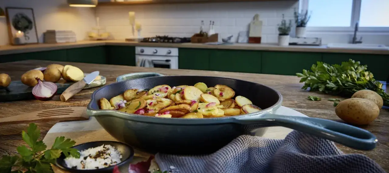 Gebratene Kartoffeln mit roten Zwiebeln und Kr&auml;utern in einer Pfanne, inspiriert von raffinierten Butter Rezepten.