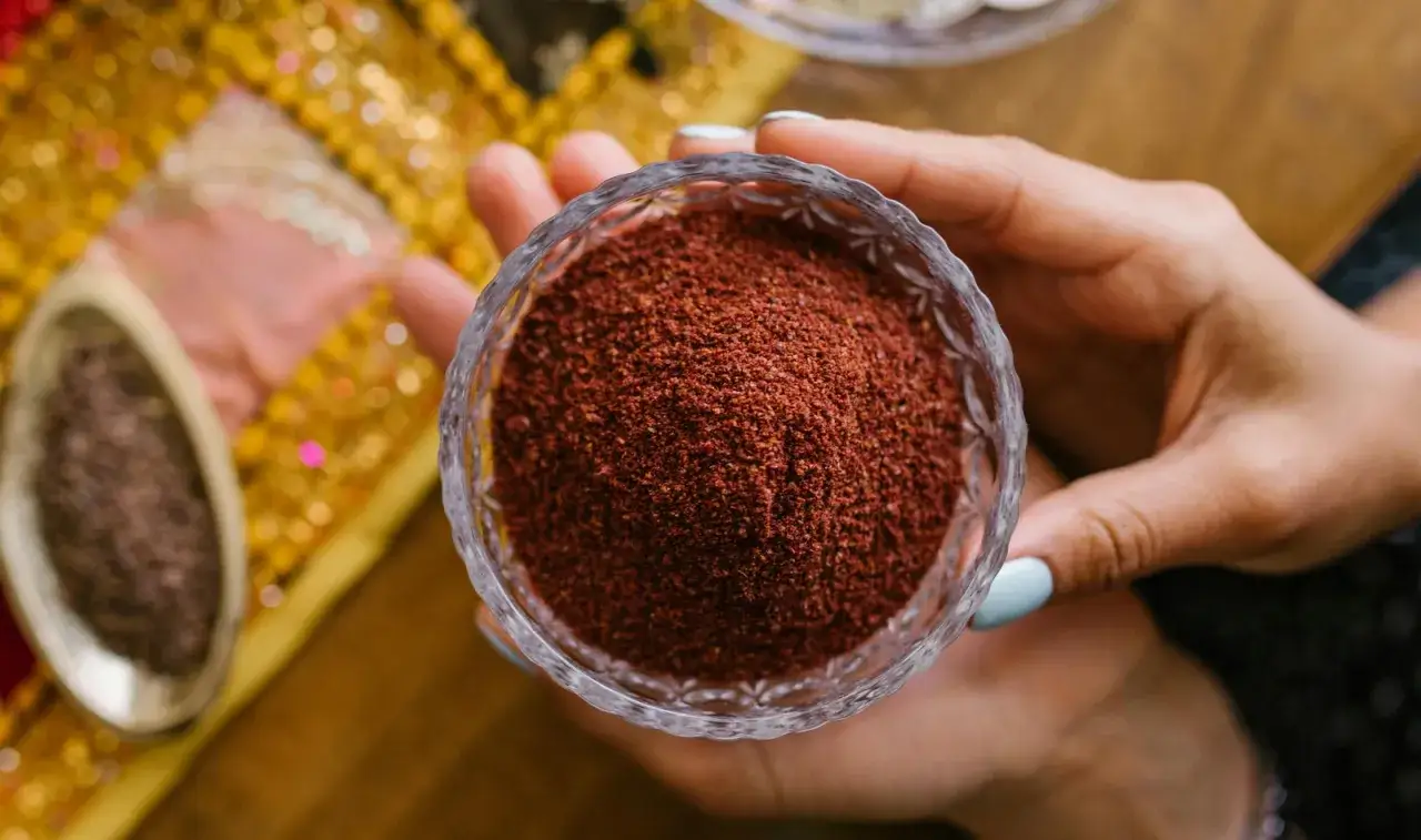 Eine Hand h&auml;lt eine Schale mit gemahlenem Sumak. Das Gew&uuml;rz hat eine tiefrote Farbe und wird oft in der orientalischen K&uuml;che verwendet.