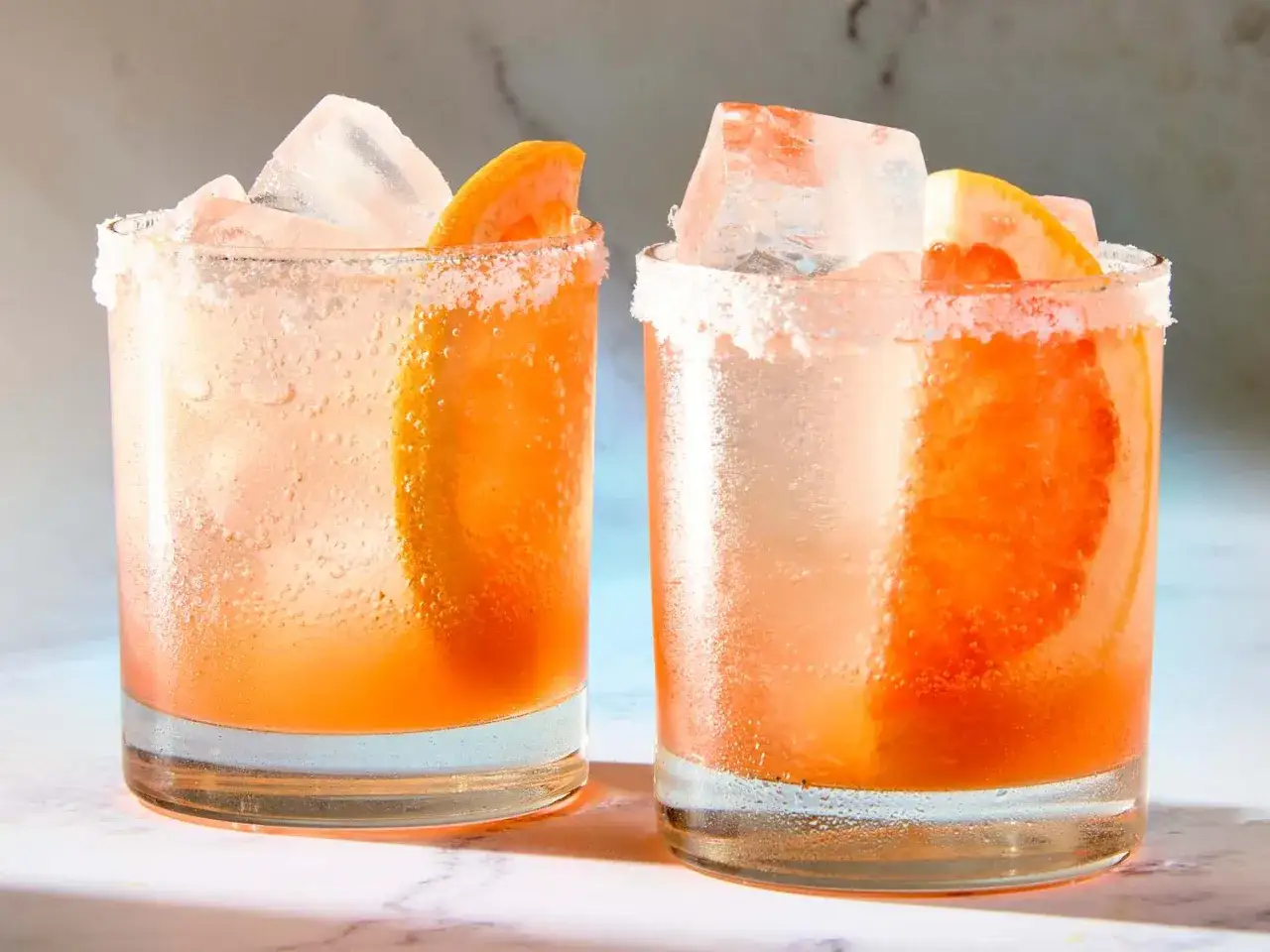 Zwei erfrischende Aperol Paloma Cocktails mit Eis und Grapefruitspalten, die Gl&auml;ser sind mit Salzrand verziert.