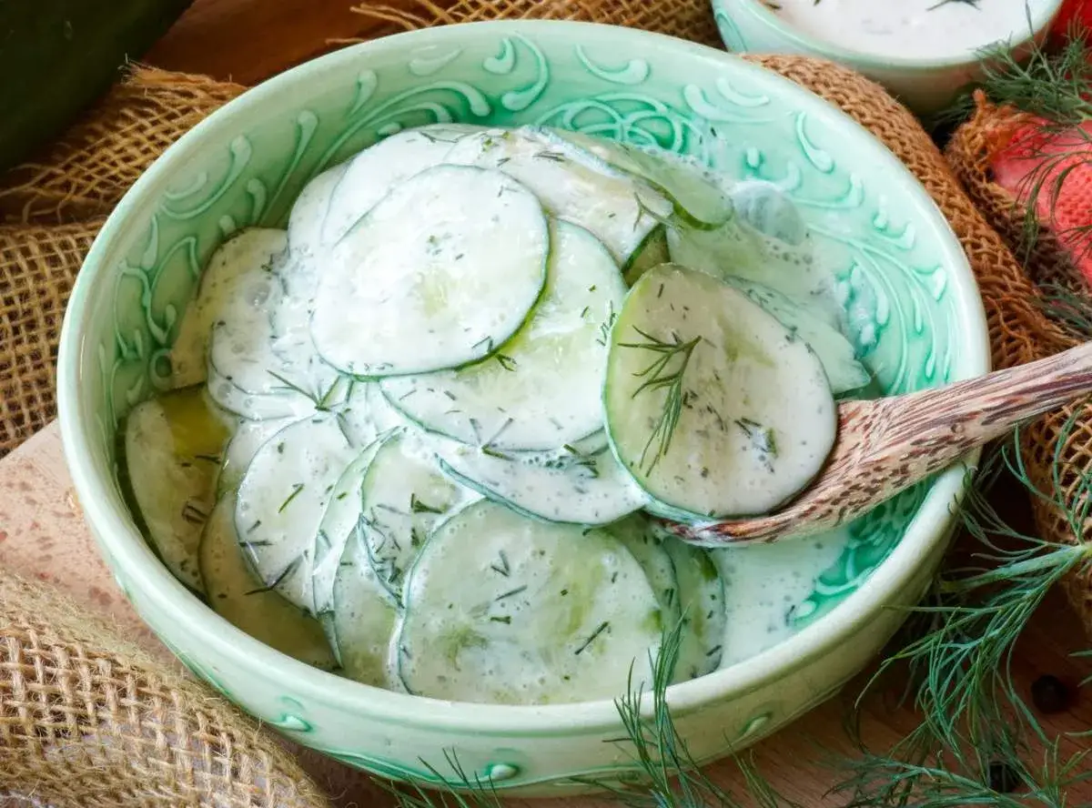 Frischer gurkensalat mit saurer sahne und dill, serviert in einer gr&uuml;nen sch&uuml;ssel.