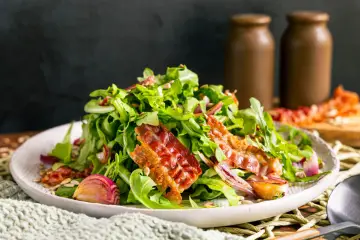 Warmer Rucolasalat mit knusprigem Speck, gerösteten Zwiebeln und Sonnenblumenkernen. Ein köstliches Gericht für Rucola Rezepte warm.