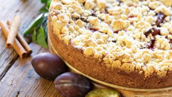 Ein saftiger Zwetschgenkuchen mit knusprigen Streuseln, daneben frische Zwetschgen und Zimtstangen. Perfekt für ein Streusel Rezept einfach!