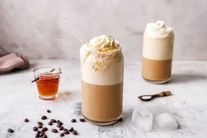Eiskaffee selbst machen: Ein erfrischender Eiskaffee mit Sahne und Sirup, daneben Kaffeebohnen und Eiswürfel.