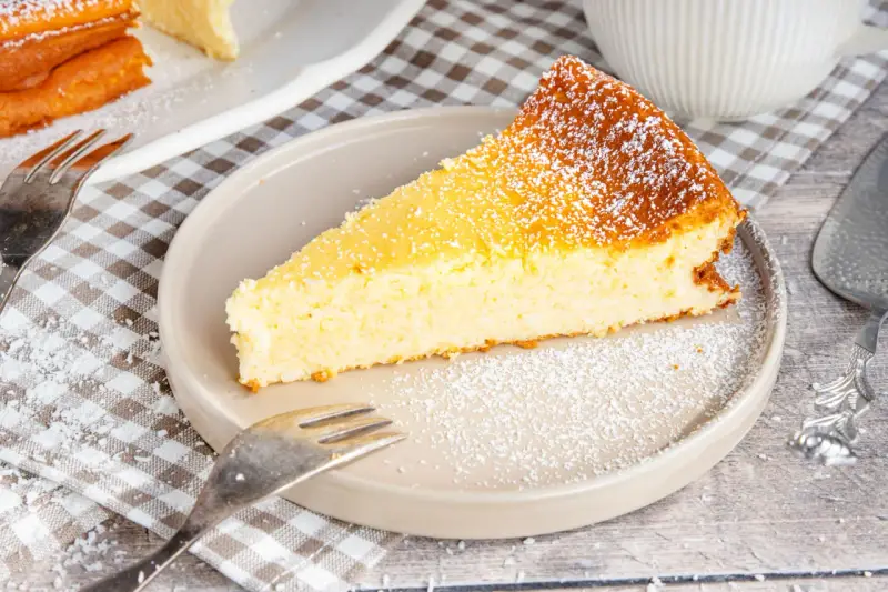 Ein saftiges Stück Kokoskuchen mit Pudding, gebacken in einer Springform, bestäubt mit Puderzucker.