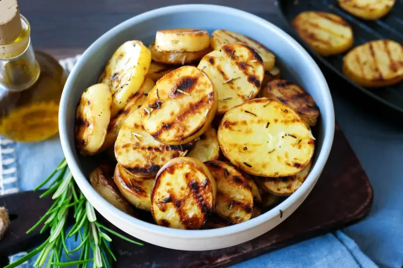 Schmackhafte Kartoffelscheiben mit Rosmarin, perfekt gegrillt. Die Streifen vom Grill sind deutlich sichtbar.